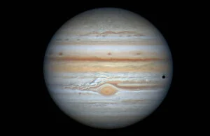 Jupiter with its orange-hued cloud bands seen through a telescope, its red spot lower centre.